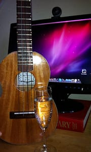 Ukulele and glass of champagne in front of computer.